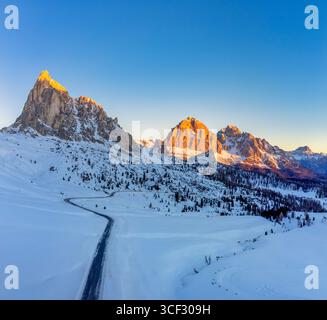 Aus der Vogelperspektive auf den Passo Giau bei Sonnenaufgang, mit der schneebedeckten Alpenstraße, die sich unterhalb von Ra Gusela windet und die Tofane-Gruppe im ersten Licht leuchtet. Dolomiten, Gemeinde Colle Santa Lucia, Provinz Belluno, Region Veneto, Italien Stockfoto