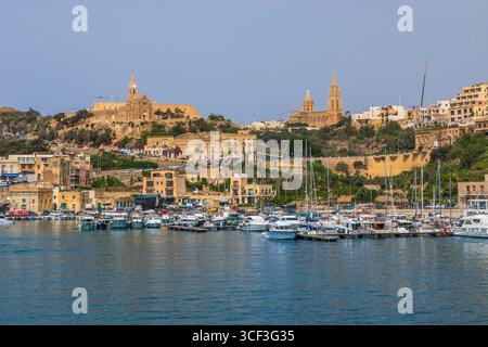 Gozo, Malta - 23. Juni 2021: Hafen mit Booten und Blick auf die Kirchen auf dem Hügel von Gozo. Stockfoto