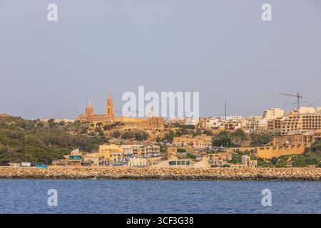 Gozo, Malta - 23. Juni 2021: Hafen mit Booten und Blick auf die Kirchen auf dem Hügel von Gozo. Stockfoto