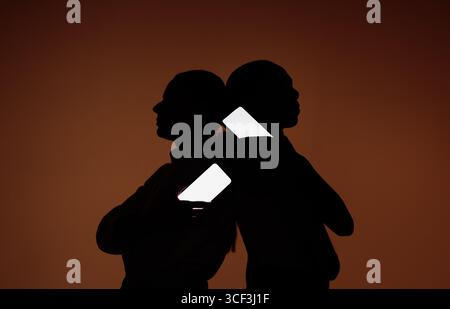 Silhouetten von zwei Personen, die Smartphones hintereinander halten, mit leuchtenden leeren Bildschirmen auf dunklem Hintergrund, ideal für mobile Mockups, soziale Medien, und Stockfoto