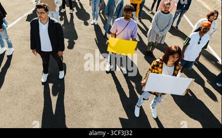 Ein Blick von oben auf eine vielfältige Menschenmenge, die zusammen steht, einige mit leeren Schildern, die Aktivismus und Einheit symbolisieren. Die Gruppe zeigt Einheit und Abschreckung Stockfoto