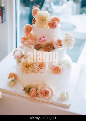 Eine atemberaubende dreistufige Hochzeitstorte mit zarten Blumendekorationen in einem hellen Rezeptionsbereich. Stockfoto