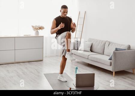 Schwarzer Mann Tut Stehende Knie Erhöhen Übung Bei Laptop Indoor Stockfoto