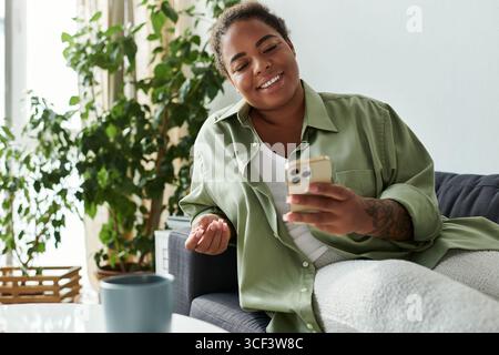 Eine afroamerikanische Frau genießt ihre Zeit zu Hause und lächelt, während sie ihr Smartphone benutzt. Stockfoto