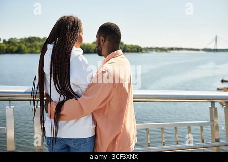 Ein junges Paar umarmt sich bei einem romantischen Spaziergang am Fluss an einem sonnigen Tag. Stockfoto
