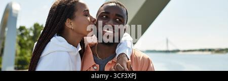 Das junge Paar genießt einen romantischen Spaziergang entlang des Flusses und teilt fröhliches Lächeln und Zuneigung. Stockfoto