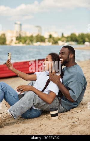 Liebevolle Paare entspannen sich am Sandstrand und fangen glückliche Erinnerungen ein, während sie Selfies machen. Stockfoto