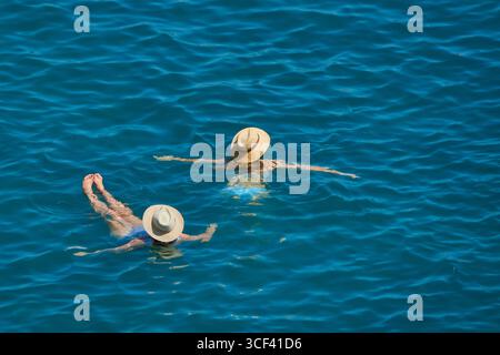 Zwei Frauen, die sich in leuchtend blauem Wasser entspannen und Strohhüte tragen Stockfoto