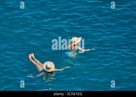 Zwei Frauen, die sich in leuchtend blauem Wasser entspannen und Strohhüte tragen Stockfoto