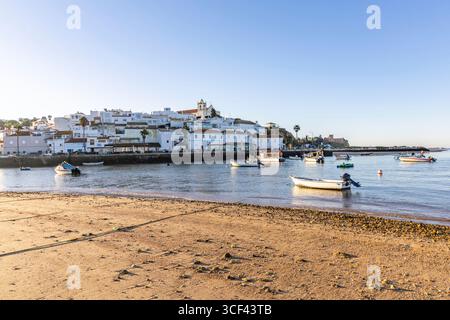 Sonnenaufgang auf dem Atlantik, Skyline eines Fischerdorfes hinter einem Hafen, Sandstrand bei Sonnenaufgang, Landschaftsaufnahmen in Ferragudo, Portimao, Algarve, Portugal Stockfoto