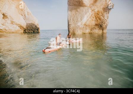 Ein Mann und eine Frau sitzen auf Surfbrettern im Meer. Der Mann trägt Shorts und die Frau trägt ein schwarzes Oberteil. Die Szene ist entspannt und sorglos Stockfoto