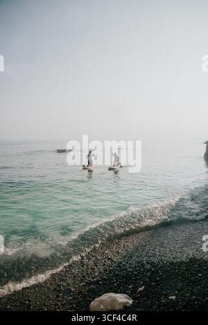 Zwei Personen Paddleboards auf einem ruhigen Meer. Der Himmel ist klar und das Wasser ist blau. Die Szene ist friedlich und entspannend Stockfoto