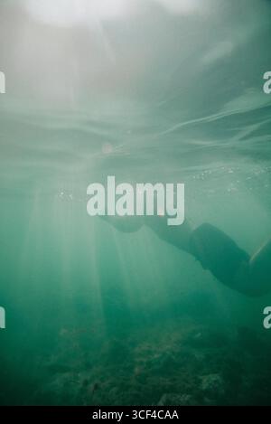 Eine Person schwimmt im Meer. Das Wasser ist grün und die Sonne scheint auf der Oberfläche Stockfoto
