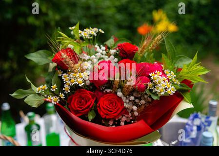Ein wunderschöner, lebendiger Blumenstrauß mit roten Rosen und weißen Blumen. Das üppige Grün und die zarten Blüten sorgen für ein perfektes Arrangement, das ideal für den Kämpfer ist Stockfoto