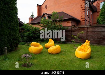 Eine ruhige Hinterhofszene mit hellgelben Sitzsäckensesseln auf üppigem grünem Gras. Umgeben von hölzernen Zäunen und lebhaften Bäumen, beginnt diese Tour Stockfoto