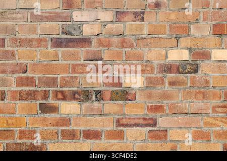 Alte Ziegelwand, Variationen in Farbe, Textur, Verschleiß, Betonung von Wiederholung und Rhythmus, enthüllen Mängel, die die Geschichte der Wand hervorheben. Stockfoto