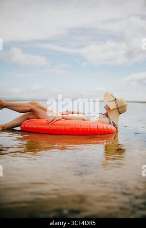 Eine Frau schwimmt auf einem roten Schlauchboot im Ozean. Die Szene ist friedlich und entspannend, die Frau genießt das Wasser und die Sonne Stockfoto