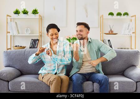 Glückliches junges Paar, das zu Hause tanzt und auf dem Sofa sitzt und eine gute Stimmung genießt. Stockfoto