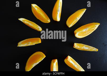 Sie können leuchtende orangefarbene Scheiben in einem kreisförmigen Muster auf tiefschwarzem Hintergrund anordnen, um einen auffälligen Kontrast zu erzeugen, der ein Gefühl von Frische und Heilung hervorruft Stockfoto