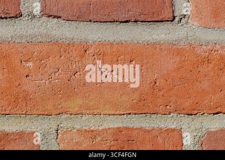 Detaillierte Ansicht einer alten roten Ziegelmauer, rauen Texturen, subtilen Rissen, verwitterten Oberflächen und einem großen zentralen Ziegelstein. Stockfoto