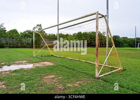 Rostiges Fußballtor mit gelbem Netz auf nassem Grasfeld. Stockfoto