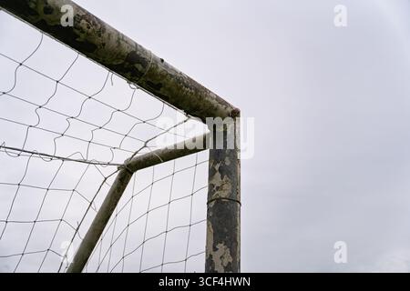 Verrostete obere Ecke eines Fußballtorpfosten mit abblätternder Farbe und abgenutztem Netz. Stockfoto