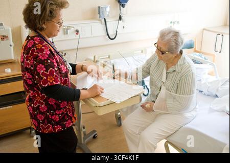 Ältere Frau Patient sitzt am Krankenhausbett Unterzeichnung Krankenhaus Entlassungspapiere Stockfoto
