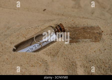 Eine Glasflasche mit einer zusammengerollten Nachricht mit Koordinaten liegt halb im Sand an einem sonnigen Strand, was auf einen verborgenen Schatz oder ein Geheimnis hindeutet Stockfoto