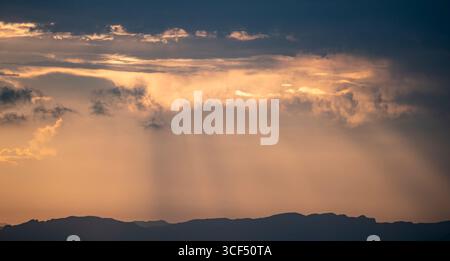 Feuriger Himmel über den Bergen bei Sonnenuntergang, mit Sonnenstrahlen, die durch die dramatischen Wolken dringen. Stockfoto