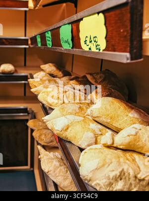 Frisch gebackene Brote in verschiedenen Formen und Größen sind auf Holzregalen in einer Bäckerei wunderschön angeordnet, wobei die Preise deutlich über die Kosten pro Kilogramm hinausgehen Stockfoto