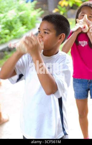 3. Grundschule Schüler hineinblasen Muschelschale als eine uralte Hawaiianische Methode immer Aufmerksamkeit und zu kommunizieren. Stockfoto