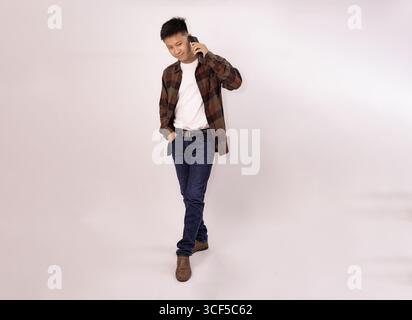 Lässiger junger Mann, der in entspannter Pose auf dem Handy spricht Stockfoto