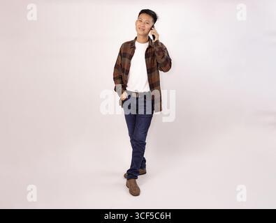 Lässiger junger Mann, der in entspannter Pose auf dem Handy spricht Stockfoto