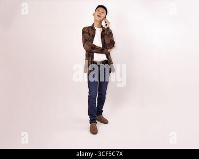 Lässiger junger Mann, der in entspannter Pose auf dem Handy spricht Stockfoto