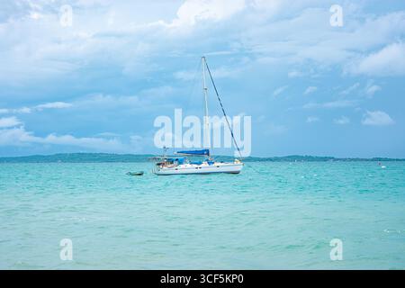Ein Segelboot vor Anker in den ruhigen Gewässern der Rosario-Inseln in der Nähe von Cartagena, Kolumbien, unter einem wunderschönen bewölkten Himmel. Stockfoto