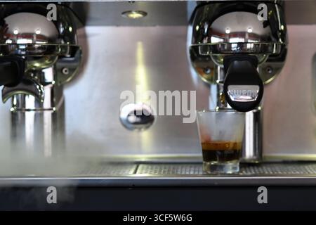 Cremona, Italien 21. Juli 2025 Wega Professional Espressomaschine für die Zubereitung von reichhaltigem Kaffee, Dampfwirbel, dunkle Flüssigkeit, die in transparentes Glas kaskadiert, ca. Stockfoto