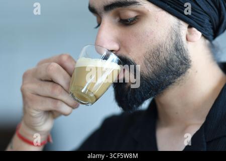 Cremona, Italien - 21. Juli 2025 Ein bärtiger Mann mit schwarzem Turban trinkt aus einem klaren Glas, gefüllt mit einem cremigen Getränk, und genießt einen Moment relaxa Stockfoto