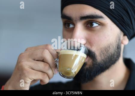 Cremona, Italien - 21. Juli 2025 Ein Sikh-Mann mit Bart und schwarzem Turban genießt drinnen eine heiße Tasse Kaffee oder Tee mit einer geringen Tiefe von Stockfoto