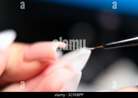 Extreme Nahaufnahme des Manikürs mit winzigem Pinsel, um gellack bei Nagelverlängerung gleichmäßig zu verteilen. Professionelle Schönheit. Stockfoto