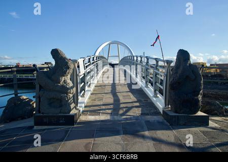 Steinmarkierungen und Geländer umrahmen den Eingang zur Bidan-Brücke in der Nähe des Hafens Geumseong, wo sich ein geschwungener weißer Bogen über die Spanne erhebt und ein gemusterter Pflaster bildet Stockfoto