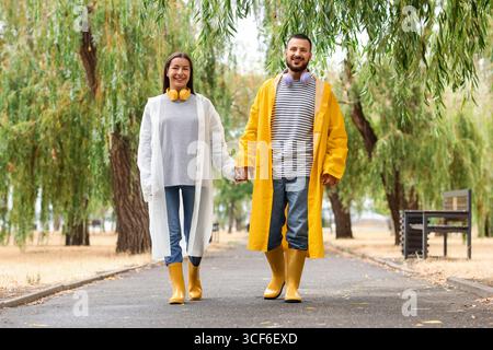 Ein junges Paar mit Regenmänteln, das im Park spaziert Stockfoto
