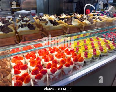 In einer italienischen Bäckerei werden verschiedene Desserts präsentiert, darunter Kuchen, Mousse und Gebäck mit Fruchtgarnitur, die in lebhaften Farben und komplizierter Handwerkskunst präsentiert werden. Stockfoto
