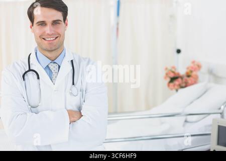 Männlicher Arzt, der am Krankenhausbett im Patientenzimmer steht und Stethoskop, Blumen, Kopierraum zeigt Stockfoto