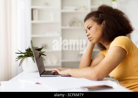 Müde afroamerikanische Frau, die mit gelangweiltem Ausdruck auf den Laptop schaut Stockfoto