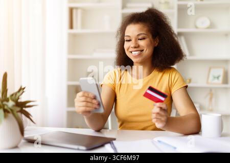 Schwarze Frau, die online mit Kreditkarte und Smartphone am Schreibtisch bezahlt Stockfoto