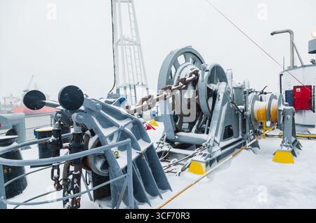 Das Anlegedeck eines Frachtschiffes mit Ankerwinden, einer Ankerkette an Winden, Pollern und Haws mit Anlegeseilen, gefroren und mit Schnee bedeckt. Sn Stockfoto