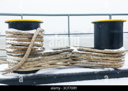 Ein Schiff im Hafen von Rotterdam bei Schneefall. Die Anlegestelle auf dem Schiffspoller ist mit Schnee bedeckt. Stockfoto