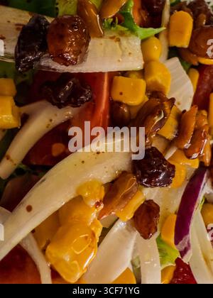 Nahaufnahme eines lebendigen gemischten Salats mit Endivien, Tomaten, Rosinen, Maiskernen, Pinienkernen, und ein leichtes Vinaigrette-Dressing Stockfoto