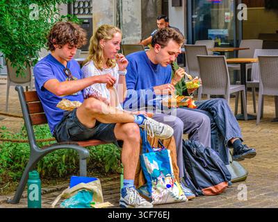 Vier junge Menschen auf einer Sitzbank essen einen Snack zum Mitnehmen in der Altstadt von Tours, Indre-et-Loire (37), Frankreich. Stockfoto