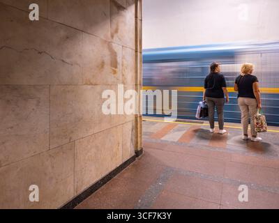 Kiew, Ukraine - 20. Juli 2025: Zwei Frauen stehen auf einem U-Bahn-Bahnsteig und warten auf einen ankommenden Zug. Sie zeigen eine Szene des täglichen Lebens im Kiewer U-Bahn-System Stockfoto